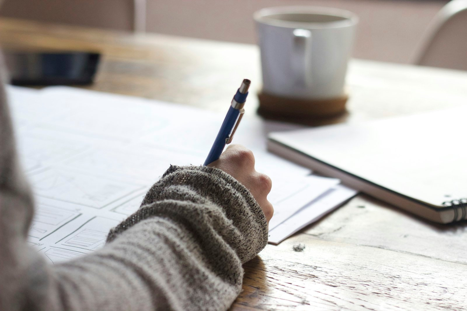 Hand schreibt Notizen neben Kaffee und Notizbuch